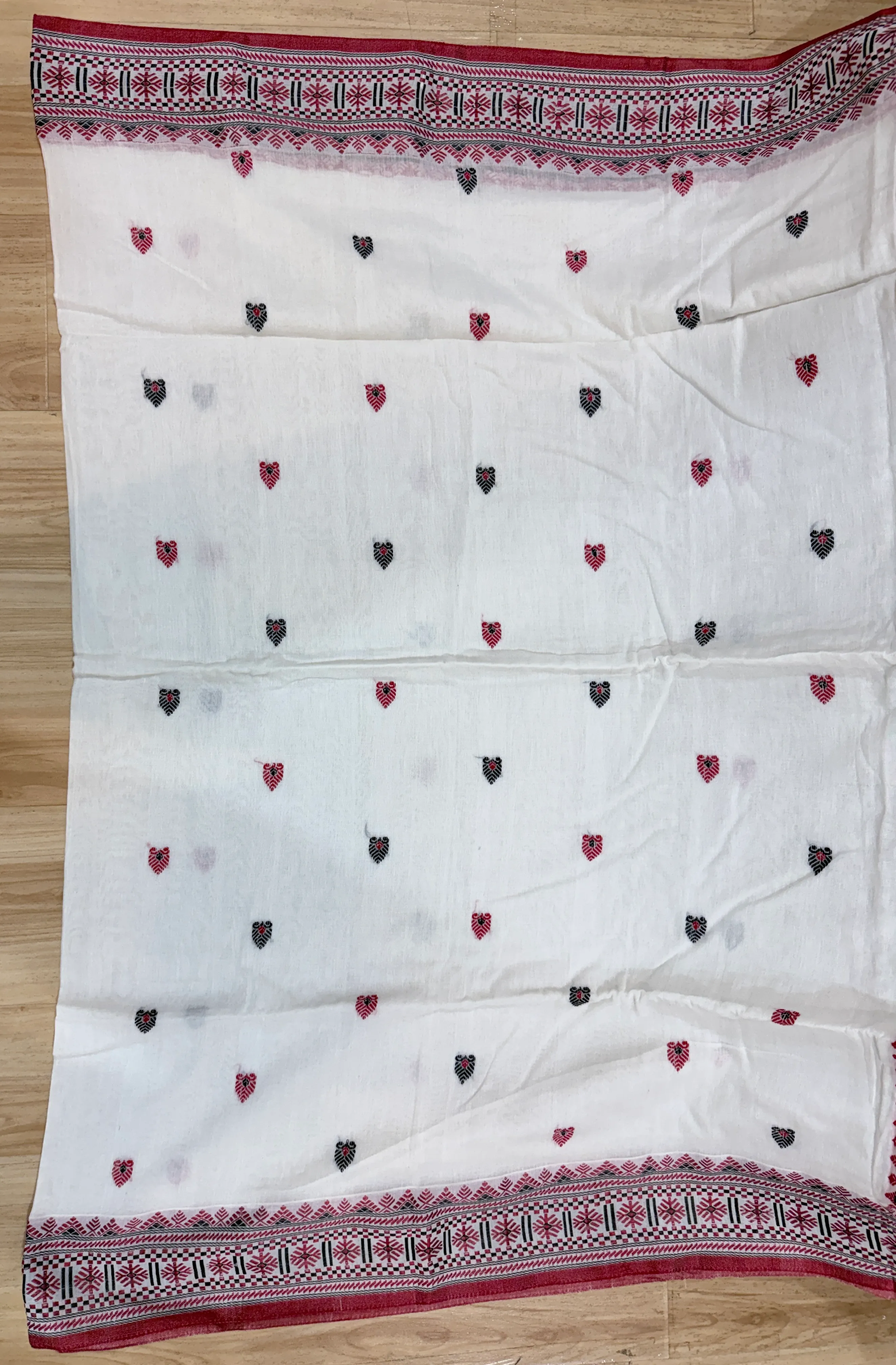 Macro shot of the Dhonekhali saree's cream field with small red and black leaf motifs scattered across the weave.
