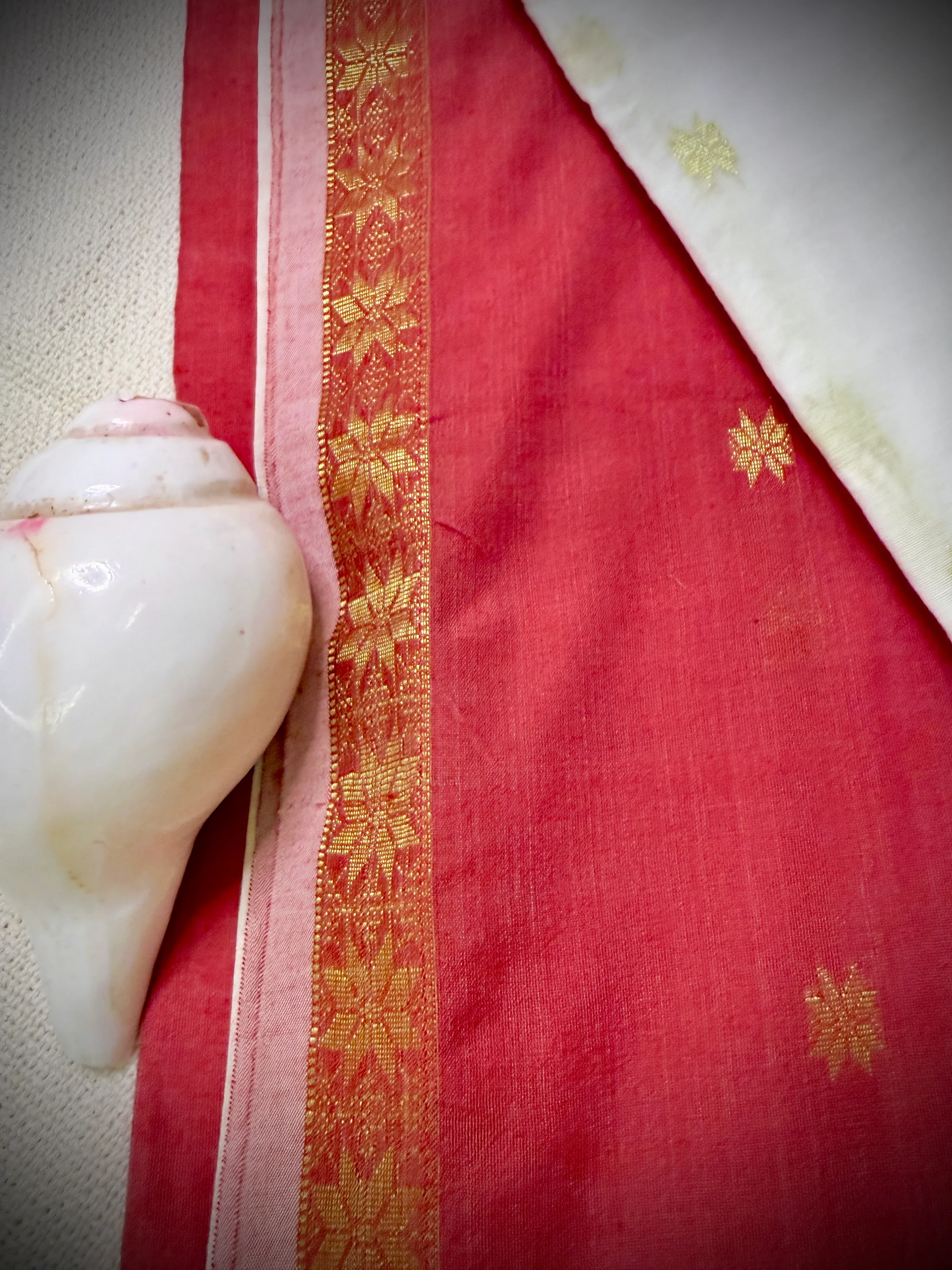 Close-up of the khadi cotton saree's gold zari border with a floral woven pattern, next to a conch shell.